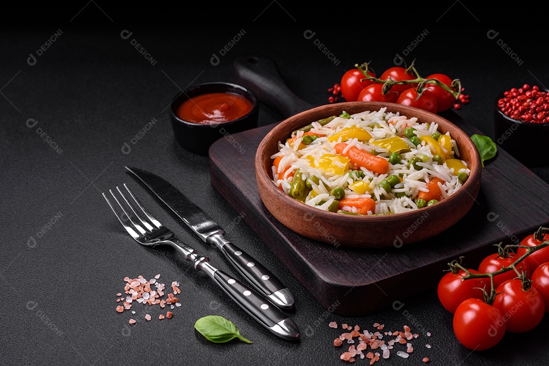 Delicioso arroz cozido branco fresco com vegetais cenouras, pimentões e feijões de espargos em uma placa cerâmica sobre um fundo escuro de concreto