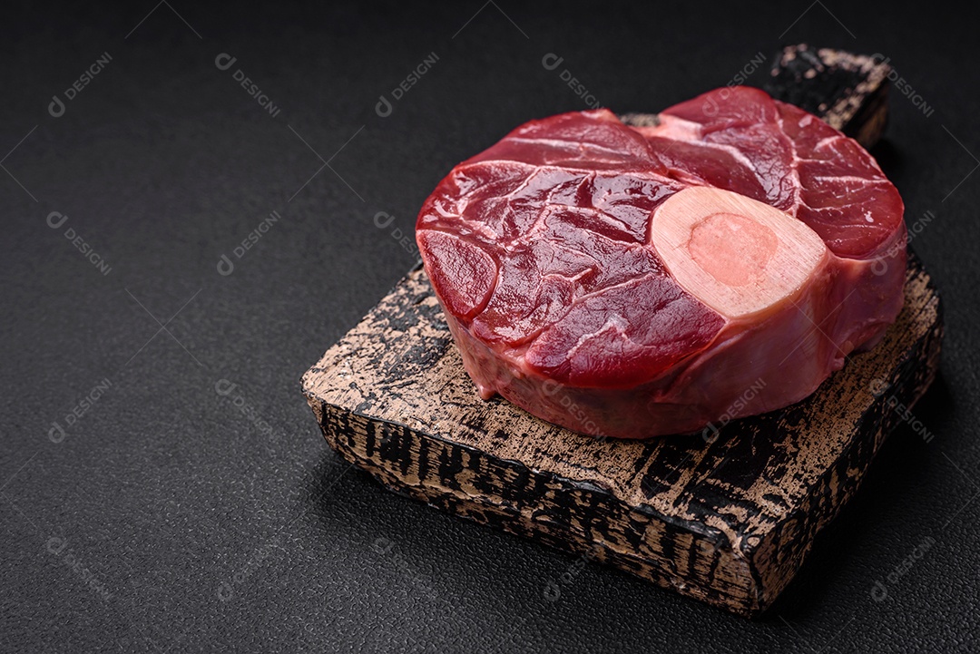 Bife cru fresco com osso ou ossobuco com sal, especiarias e ervas em fundo escuro de concreto