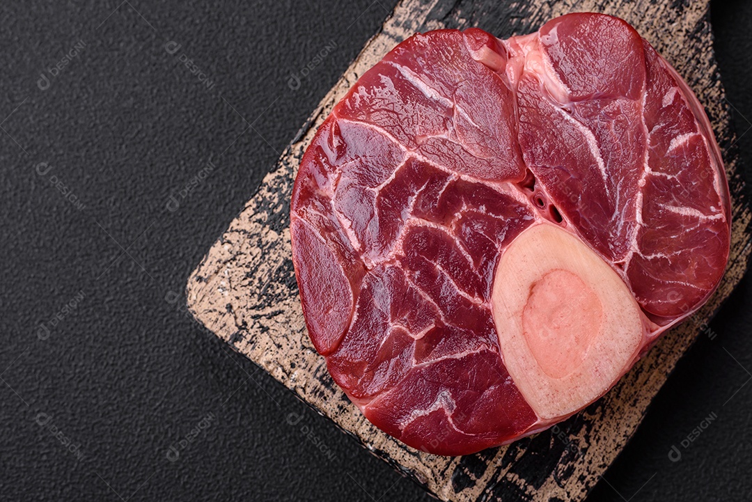 Bife cru fresco com osso ou ossobuco com sal, especiarias e ervas em fundo escuro de concreto