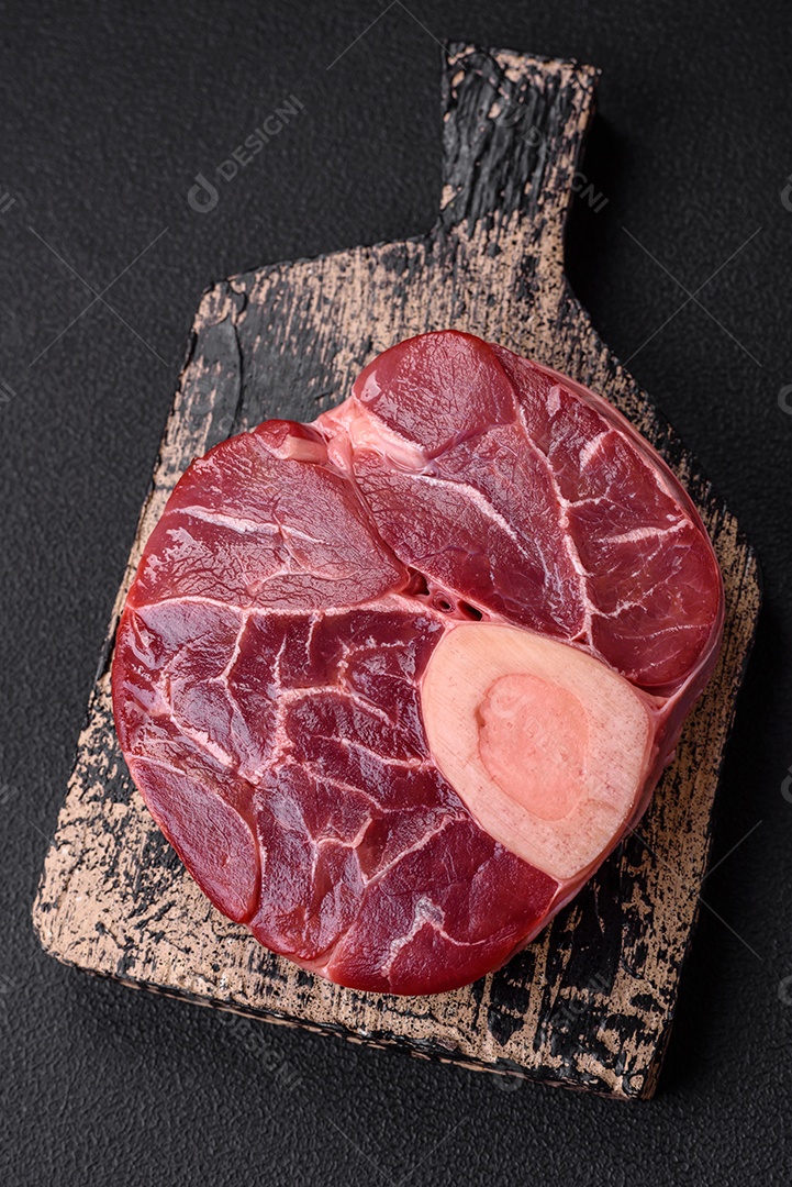 Bife cru fresco com osso ou ossobuco com sal, especiarias e ervas em fundo escuro de concreto