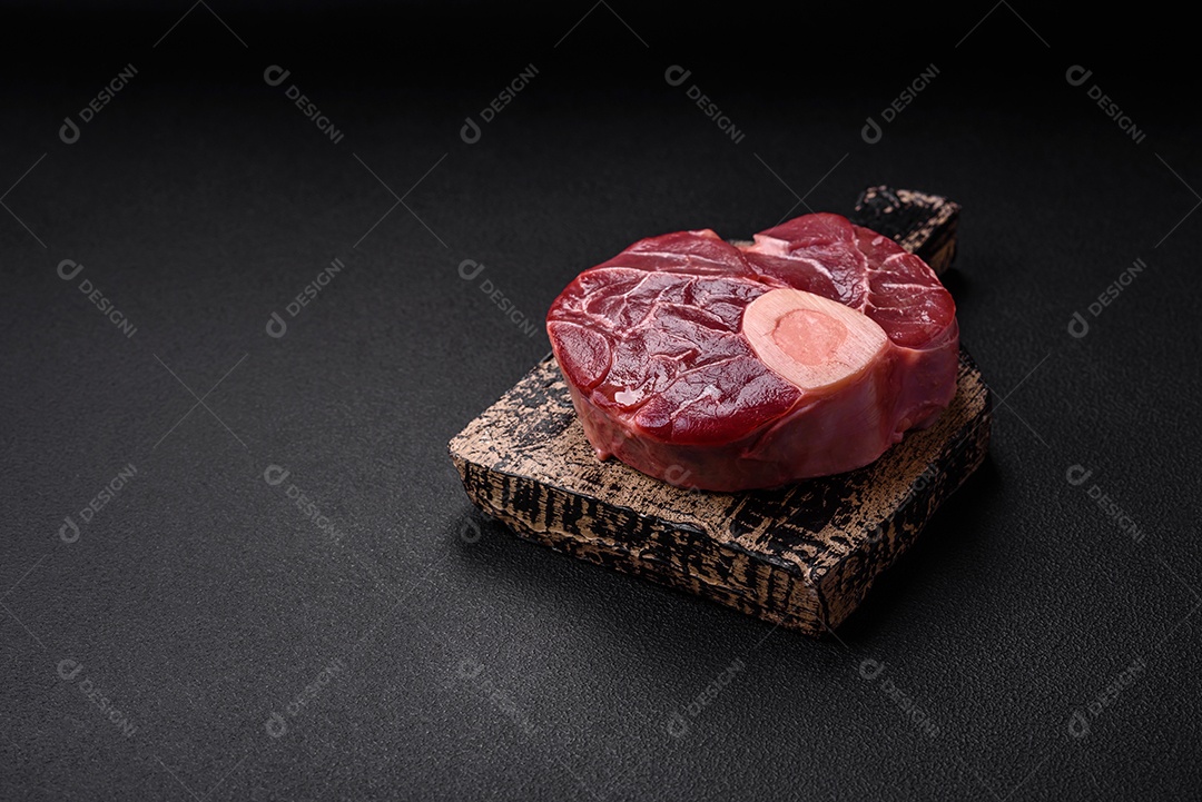 Bife cru fresco com osso ou ossobuco com sal, especiarias e ervas em fundo escuro de concreto
