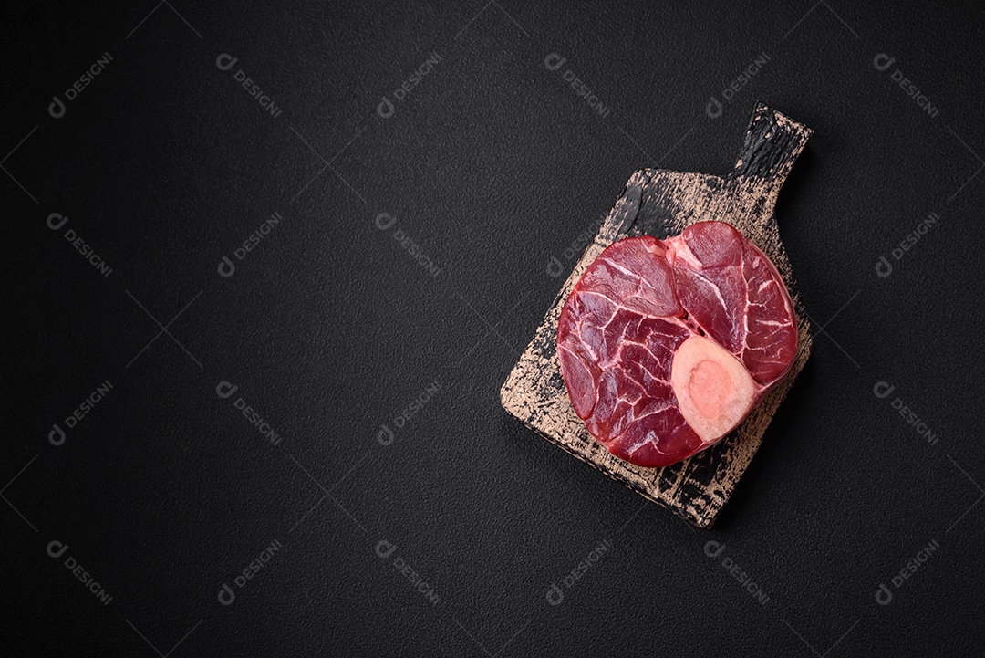 Bife cru fresco com osso ou ossobuco com sal, especiarias e ervas em fundo escuro de concreto