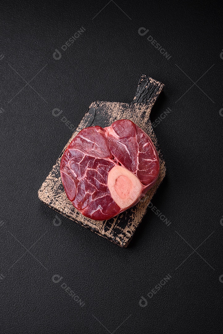 Bife cru fresco com osso ou ossobuco com sal, especiarias e ervas em fundo escuro de concreto