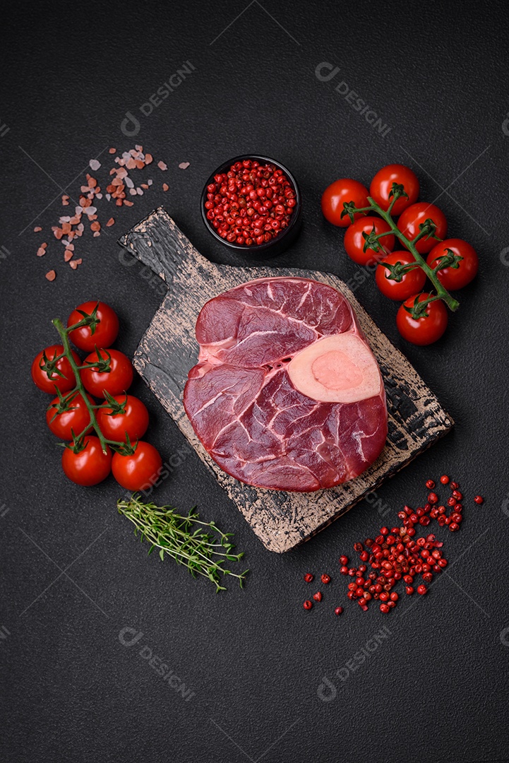 Bife cru fresco com osso ou ossobuco com sal, especiarias e ervas em fundo escuro de concreto