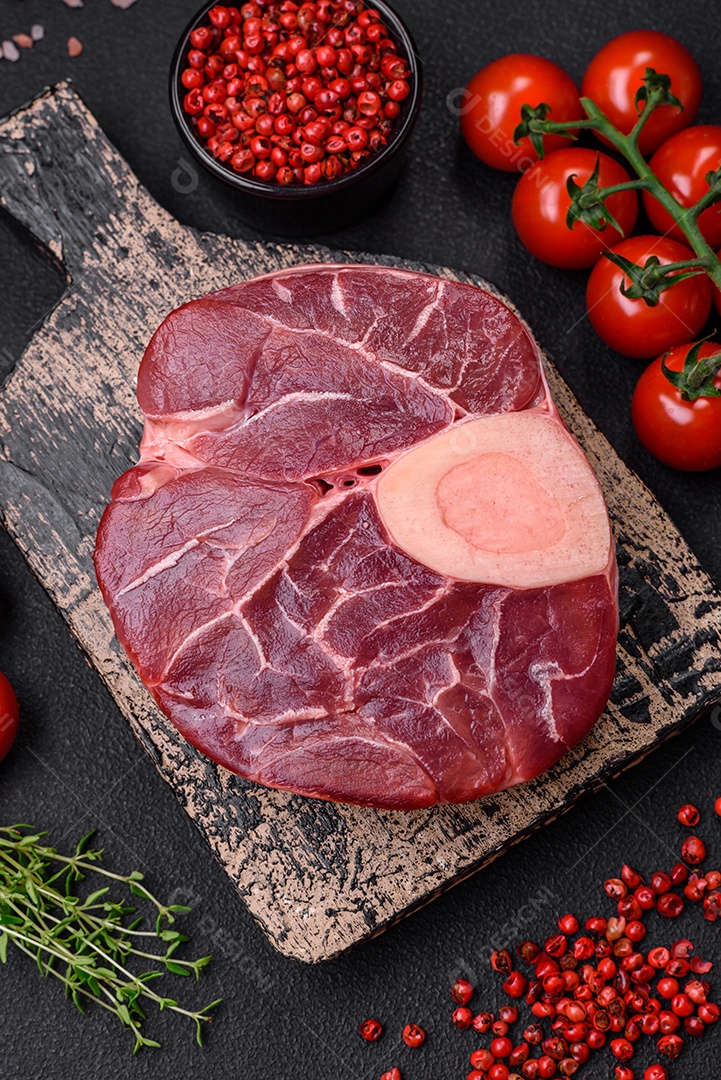 Bife cru fresco com osso ou ossobuco com sal, especiarias e ervas em fundo escuro de concreto