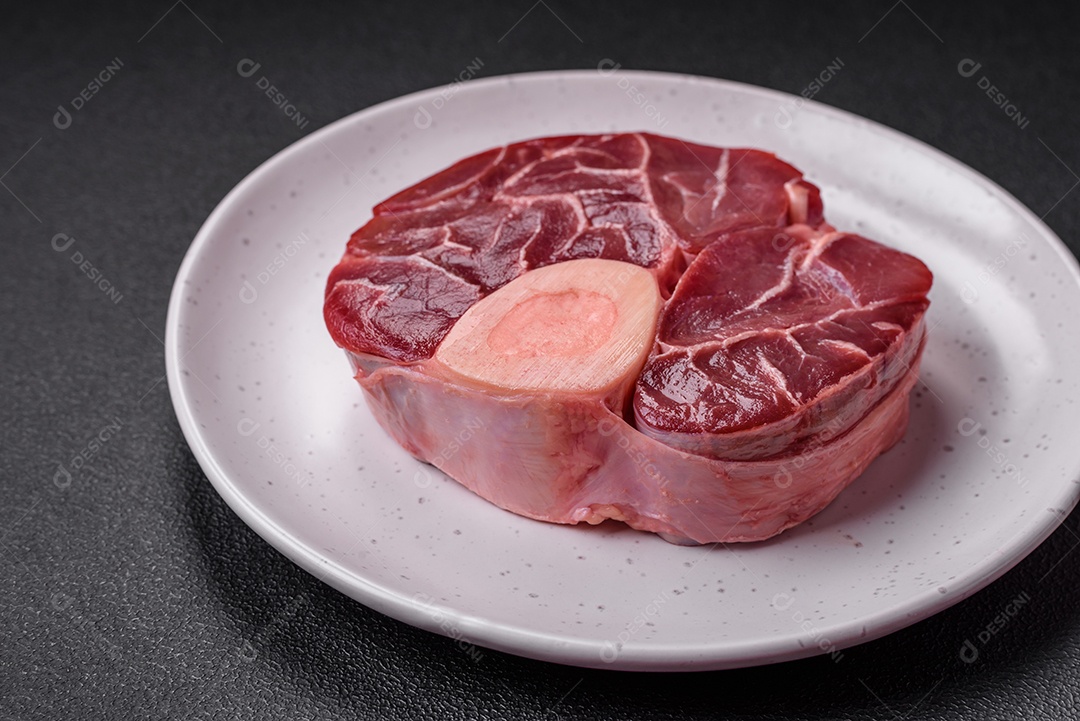 Bife cru fresco com osso ou ossobuco com sal, especiarias e ervas em fundo escuro de concreto
