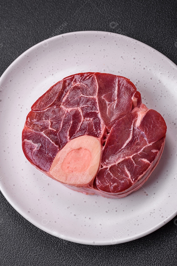 Bife cru fresco com osso ou ossobuco com sal, especiarias e ervas em fundo escuro de concreto