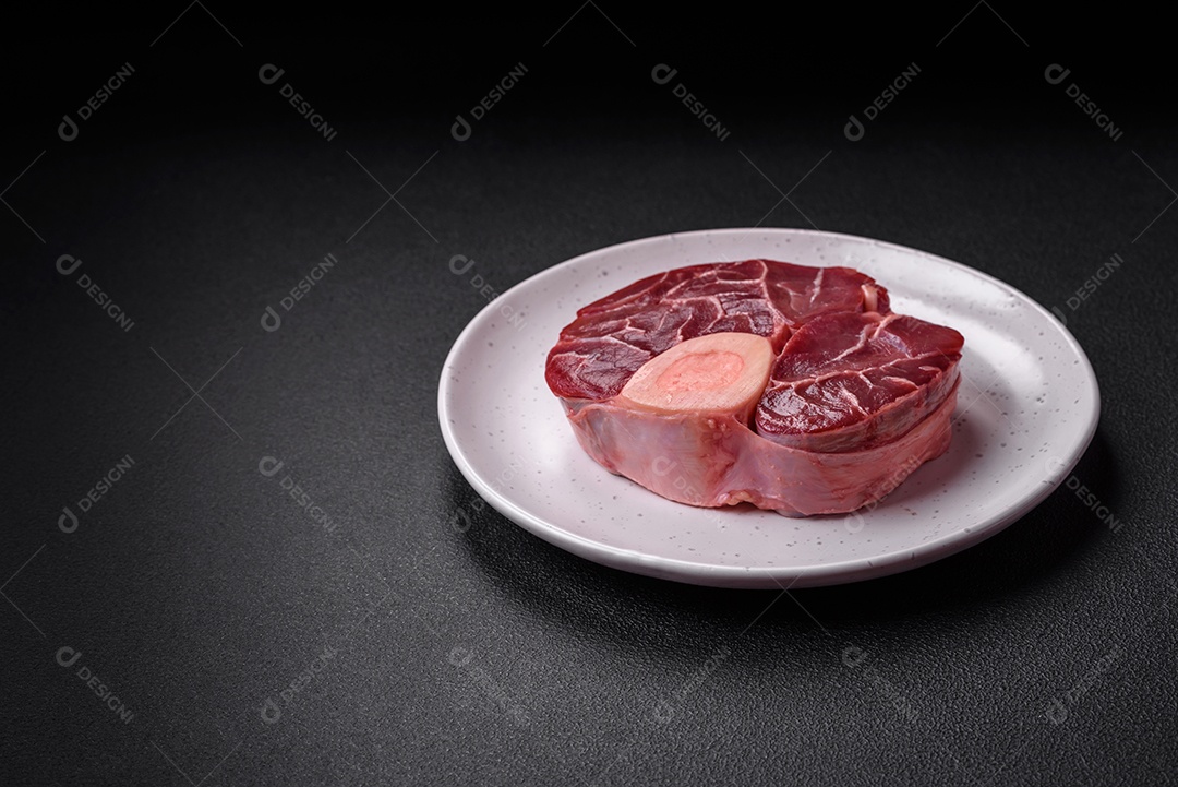 Bife cru fresco com osso ou ossobuco com sal, especiarias e ervas em fundo escuro de concreto