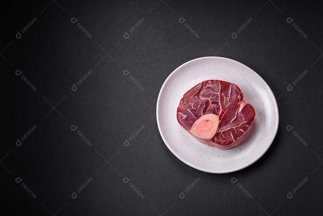 Bife cru fresco com osso ou ossobuco com sal, especiarias e ervas em fundo escuro de concreto