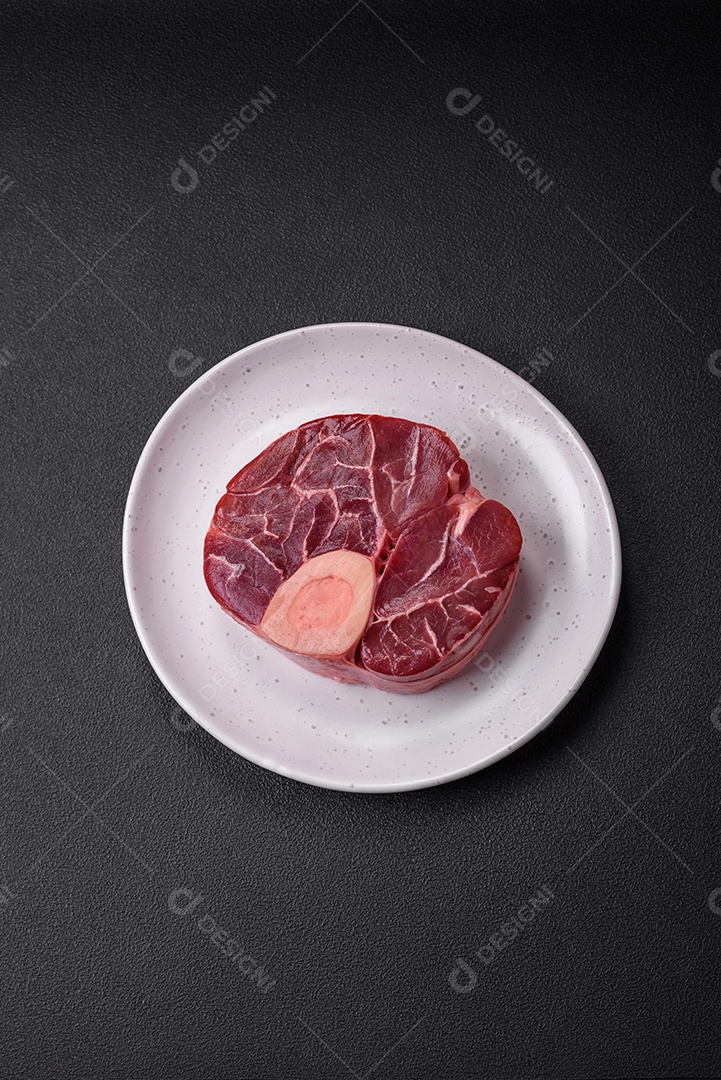 Bife cru fresco com osso ou ossobuco com sal, especiarias e ervas em fundo escuro de concreto