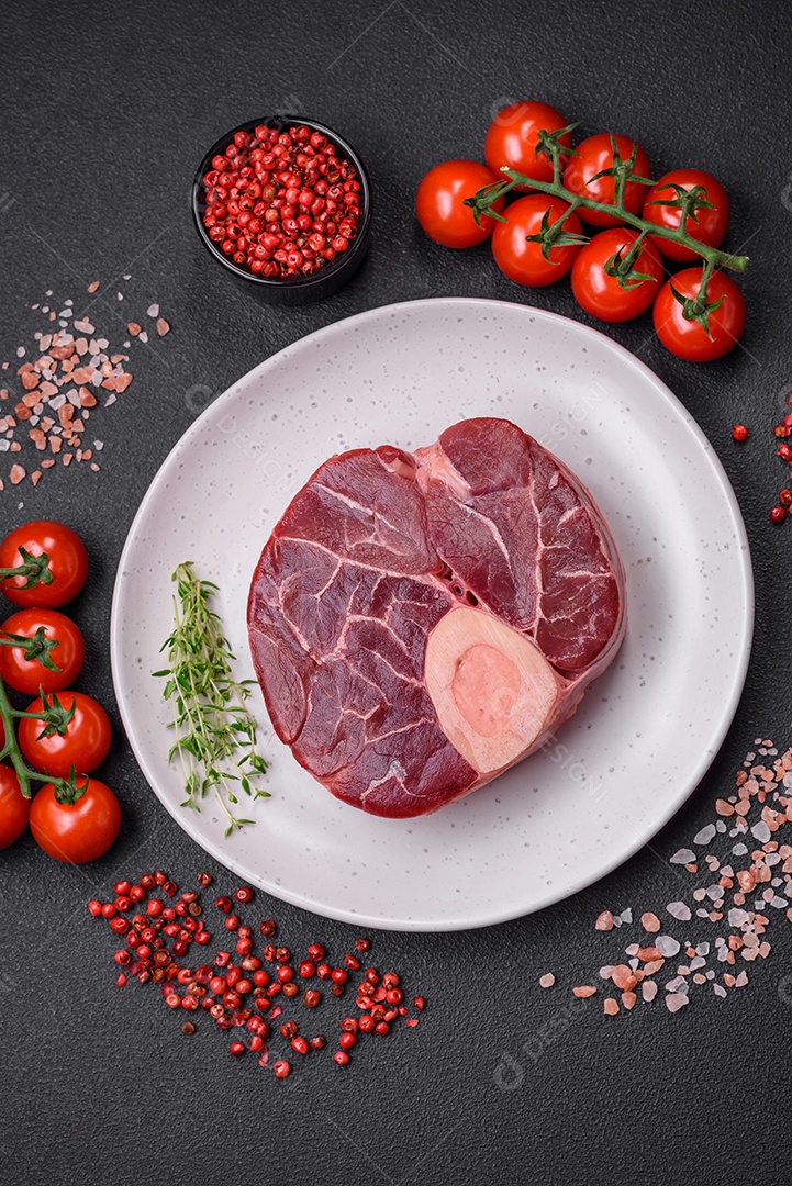 Bife cru fresco com osso ou ossobuco com sal, especiarias e ervas em fundo escuro de concreto