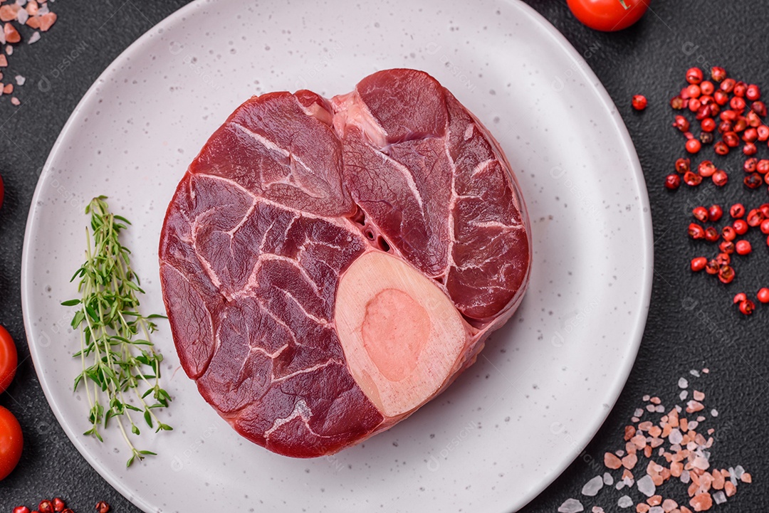 Bife cru fresco com osso ou ossobuco com sal, especiarias e ervas em fundo escuro de concreto
