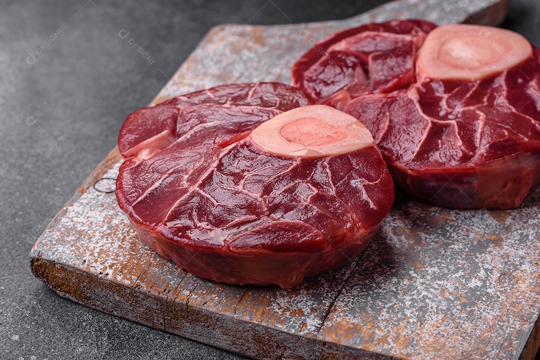 Bife cru fresco com osso ou ossobuco com sal, especiarias e ervas em fundo escuro de concreto