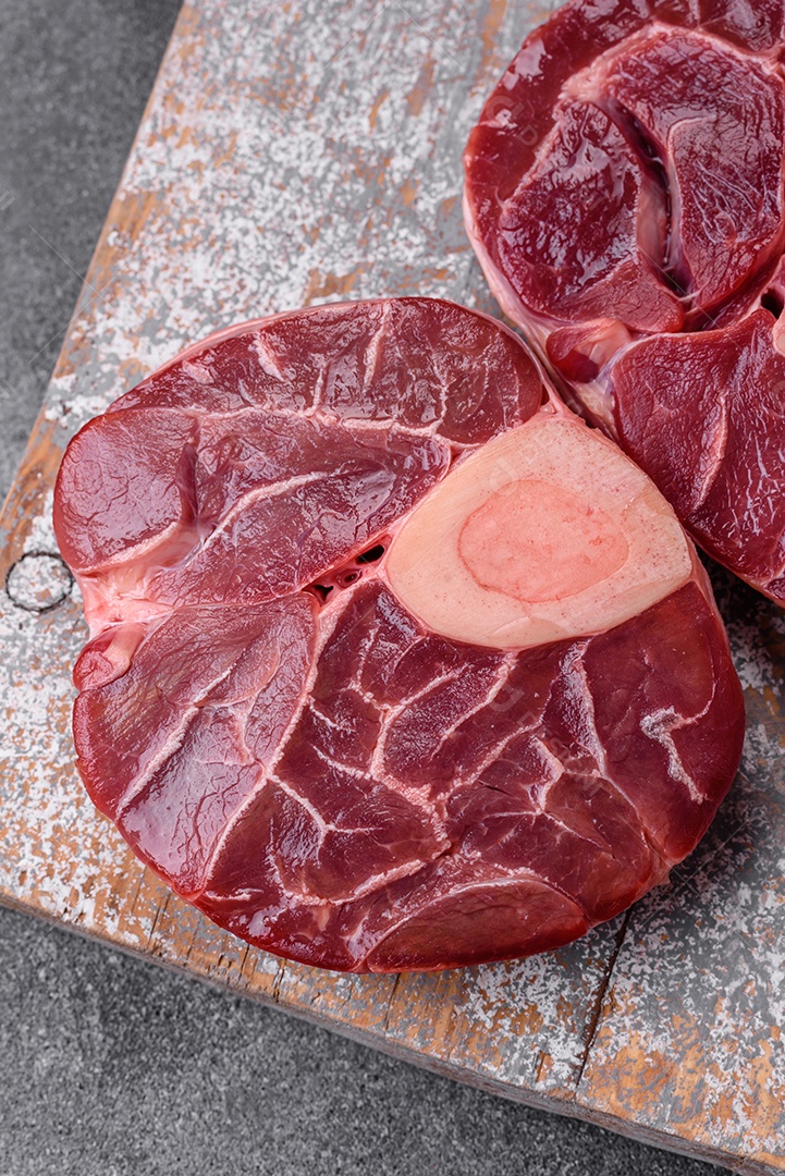 Bife cru fresco com osso ou ossobuco com sal, especiarias e ervas em fundo escuro de concreto