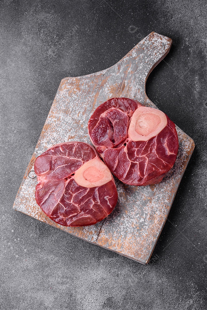 Bife cru fresco com osso ou ossobuco com sal, especiarias e ervas em fundo escuro de concreto