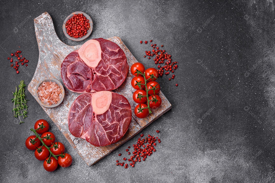 Bife cru fresco com osso ou ossobuco com sal, especiarias e ervas em fundo escuro de concreto
