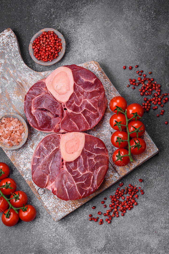 Bife cru fresco com osso ou ossobuco com sal, especiarias e ervas em fundo escuro de concreto