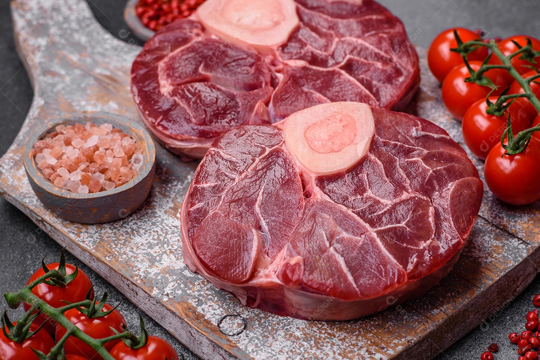 Bife cru fresco com osso ou ossobuco com sal, especiarias e ervas em fundo escuro de concreto