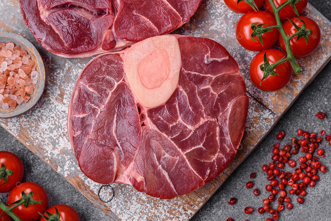 Bife cru fresco com osso ou ossobuco com sal, especiarias e ervas em fundo escuro de concreto