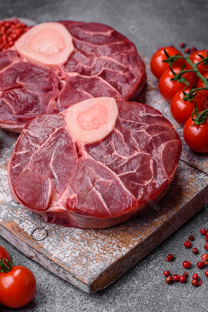 Bife cru fresco com osso ou ossobuco com sal, especiarias e ervas em fundo escuro de concreto