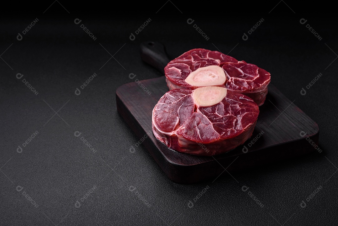Bife cru fresco com osso ou ossobuco com sal, especiarias e ervas em fundo escuro de concreto