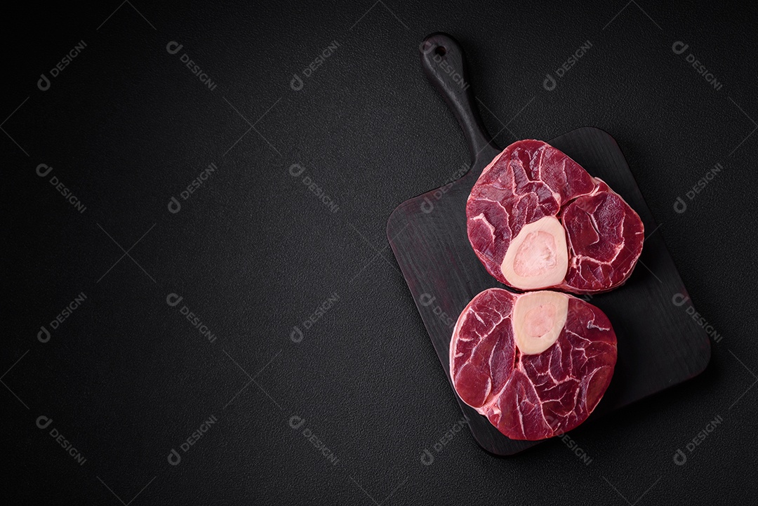 Bife cru fresco com osso ou ossobuco com sal, especiarias e ervas em fundo escuro de concreto