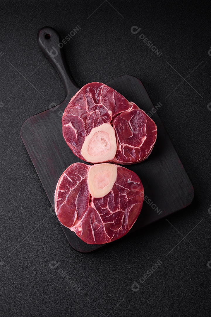 Bife cru fresco com osso ou ossobuco com sal, especiarias e ervas em fundo escuro de concreto