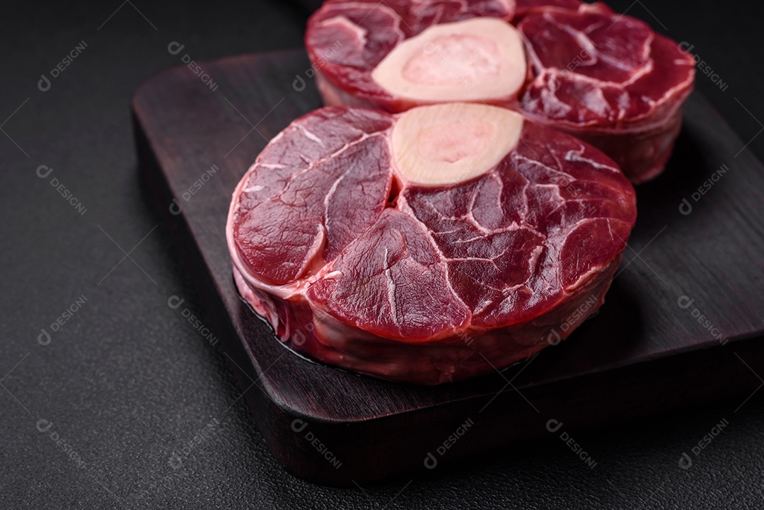 Bife cru fresco com osso ou ossobuco com sal, especiarias e ervas em fundo escuro de concreto