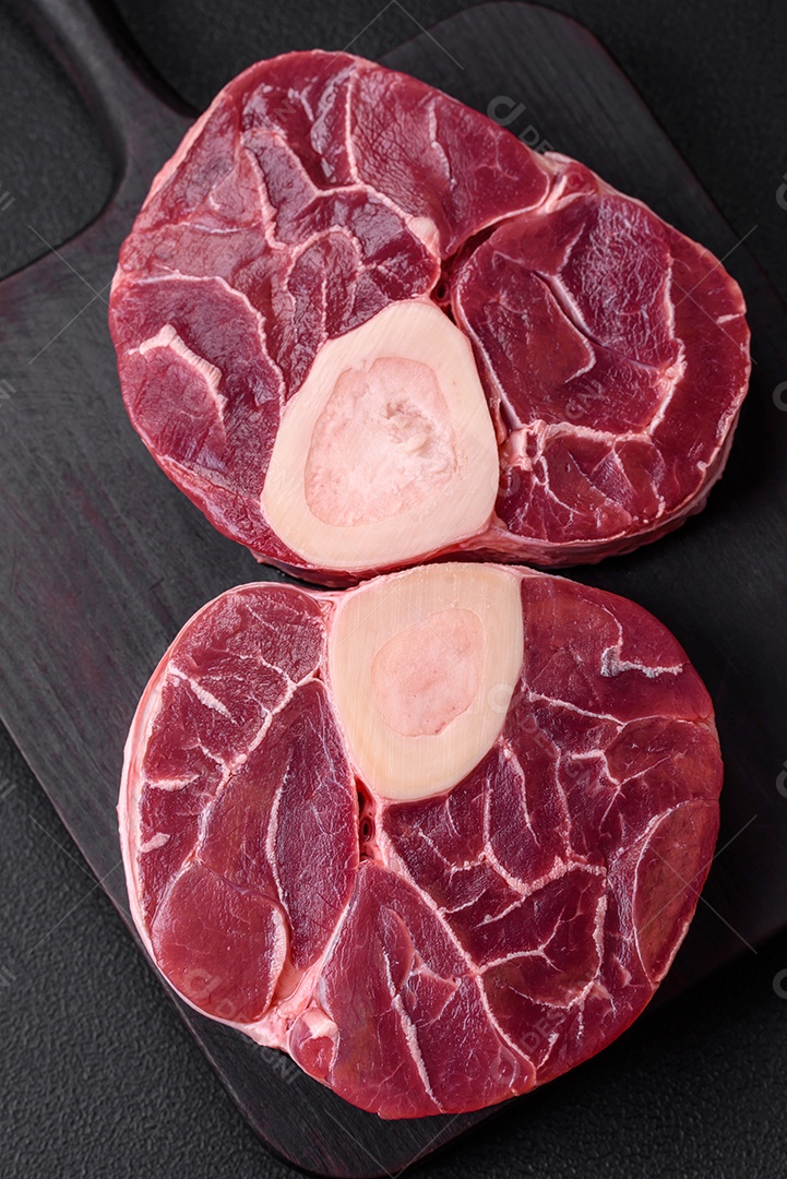 Bife cru fresco com osso ou ossobuco com sal, especiarias e ervas em fundo escuro de concreto