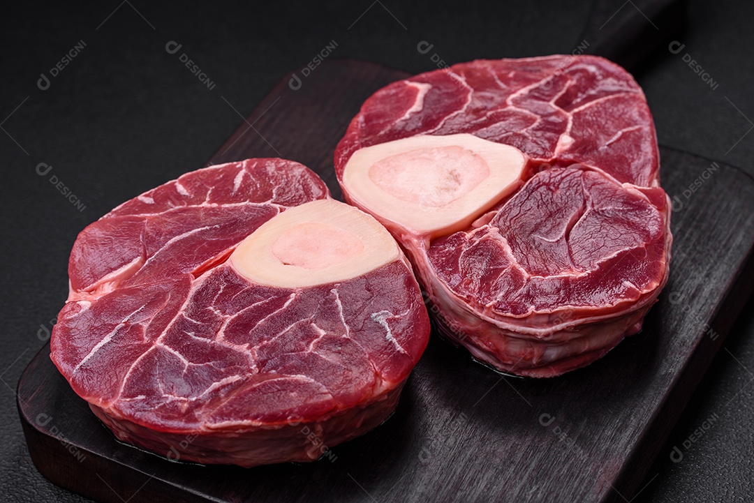 Bife cru fresco com osso ou ossobuco com sal, especiarias e ervas em fundo escuro de concreto