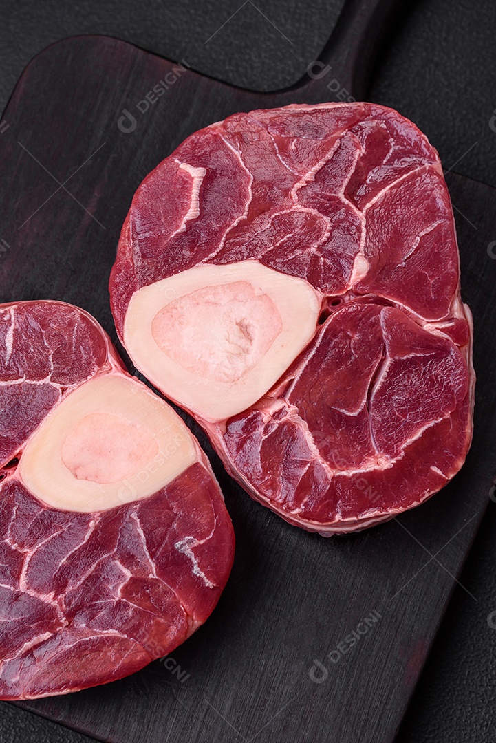 Bife cru fresco com osso ou ossobuco com sal, especiarias e ervas em fundo escuro de concreto