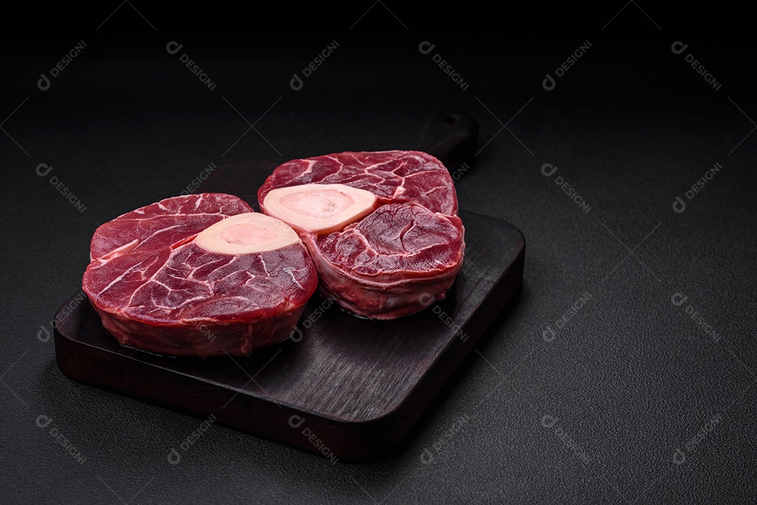 Bife cru fresco com osso ou ossobuco com sal, especiarias e ervas em fundo escuro de concreto
