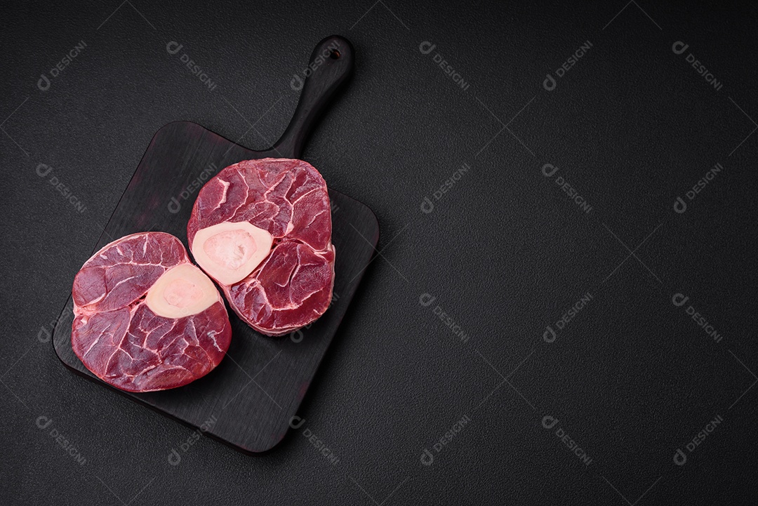 Bife cru fresco com osso ou ossobuco com sal, especiarias e ervas em fundo escuro de concreto