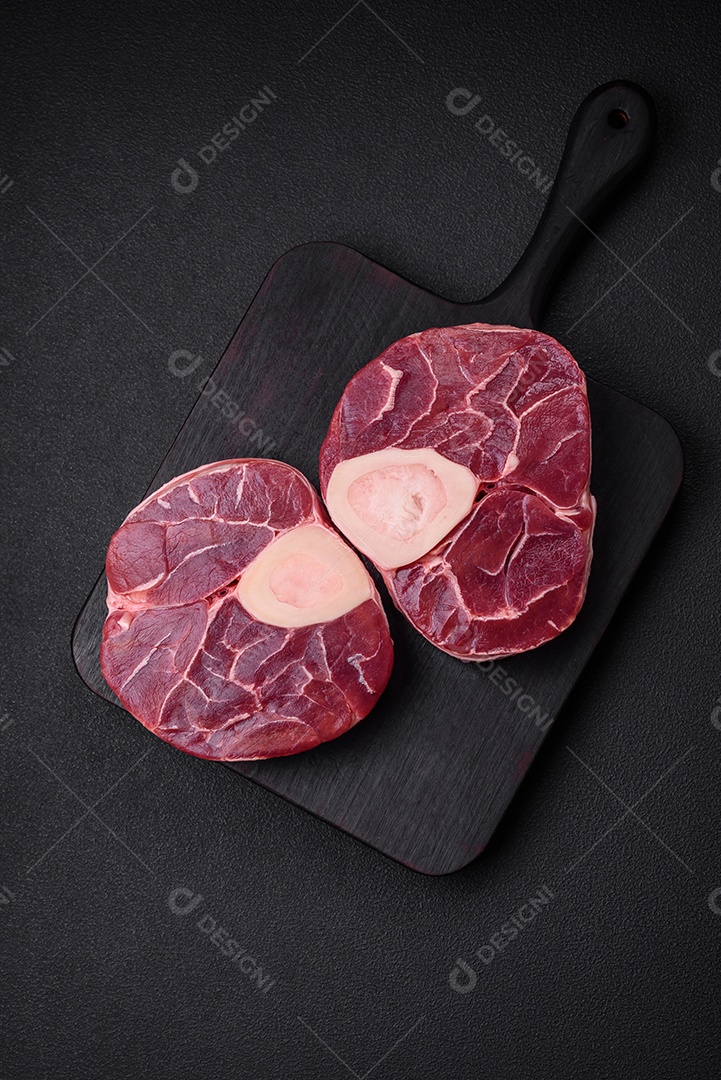 Bife cru fresco com osso ou ossobuco com sal, especiarias e ervas em fundo escuro de concreto