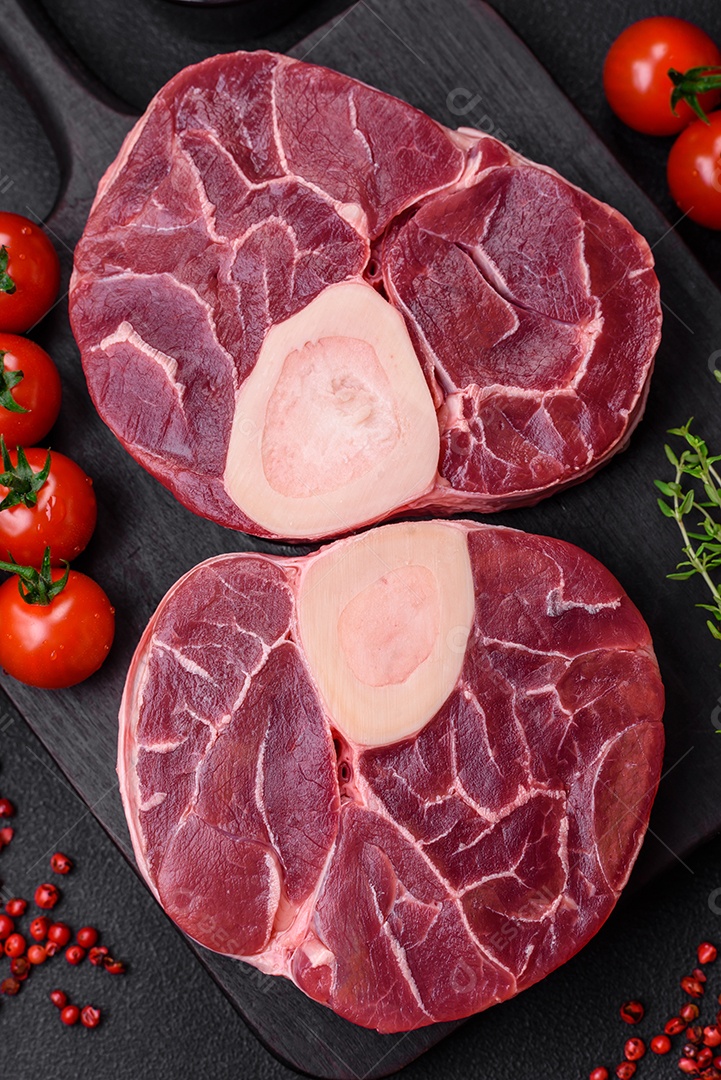 Bife cru fresco com osso ou ossobuco com sal, especiarias e ervas em fundo escuro de concreto