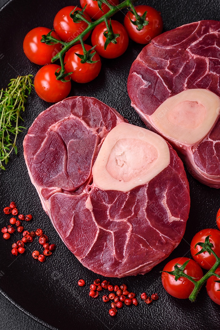 Bife cru fresco com osso ou ossobuco com sal, especiarias e ervas em fundo escuro de concreto