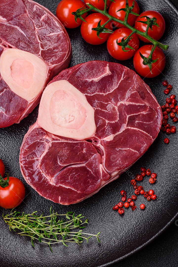 Bife cru fresco com osso ou ossobuco com sal, especiarias e ervas em fundo escuro de concreto