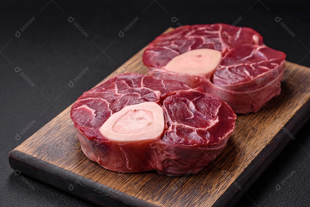 Bife cru fresco com osso ou ossobuco com sal, especiarias e ervas em fundo escuro de concreto
