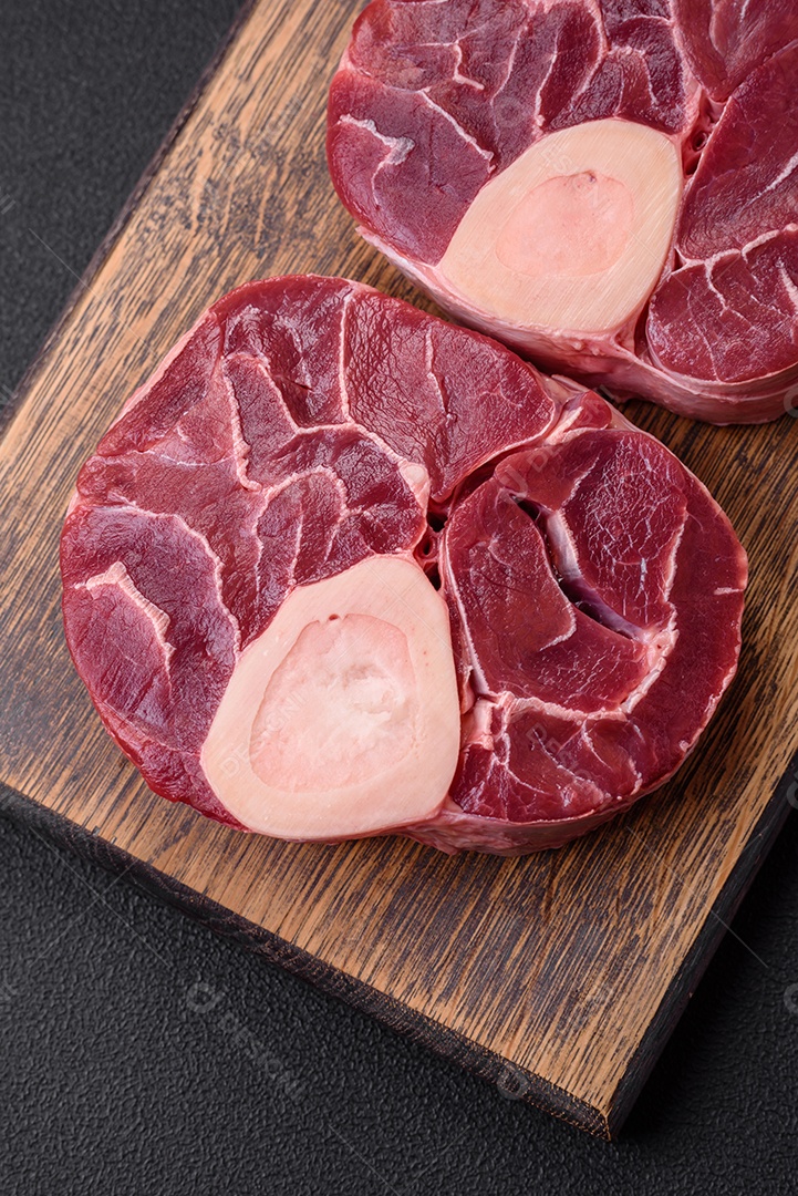 Bife cru fresco com osso ou ossobuco com sal, especiarias e ervas em fundo escuro de concreto