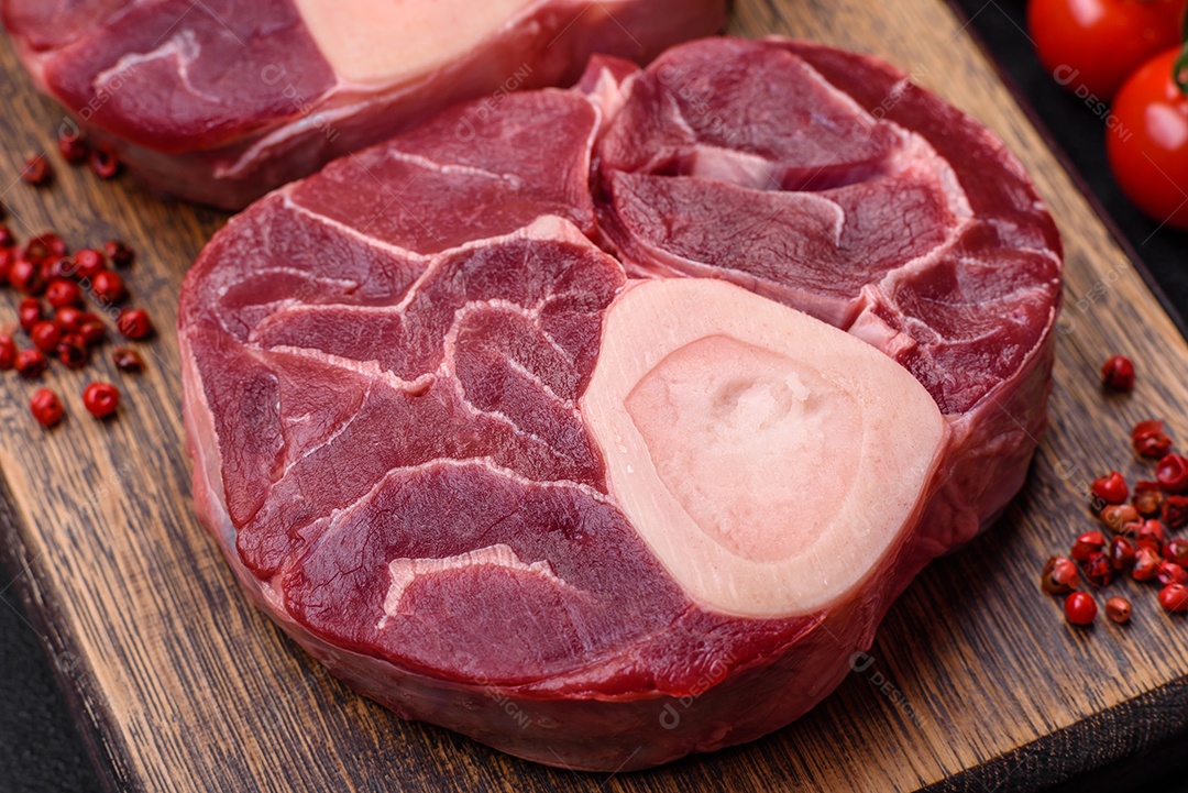 Bife cru fresco com osso ou ossobuco com sal, especiarias e ervas em fundo escuro de concreto