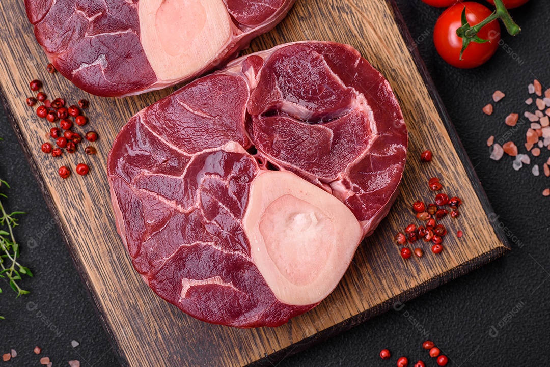 Bife cru fresco com osso ou ossobuco com sal, especiarias e ervas em fundo escuro de concreto