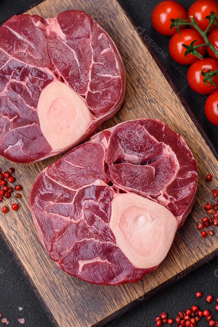 Bife cru fresco com osso ou ossobuco com sal, especiarias e ervas em fundo escuro de concreto