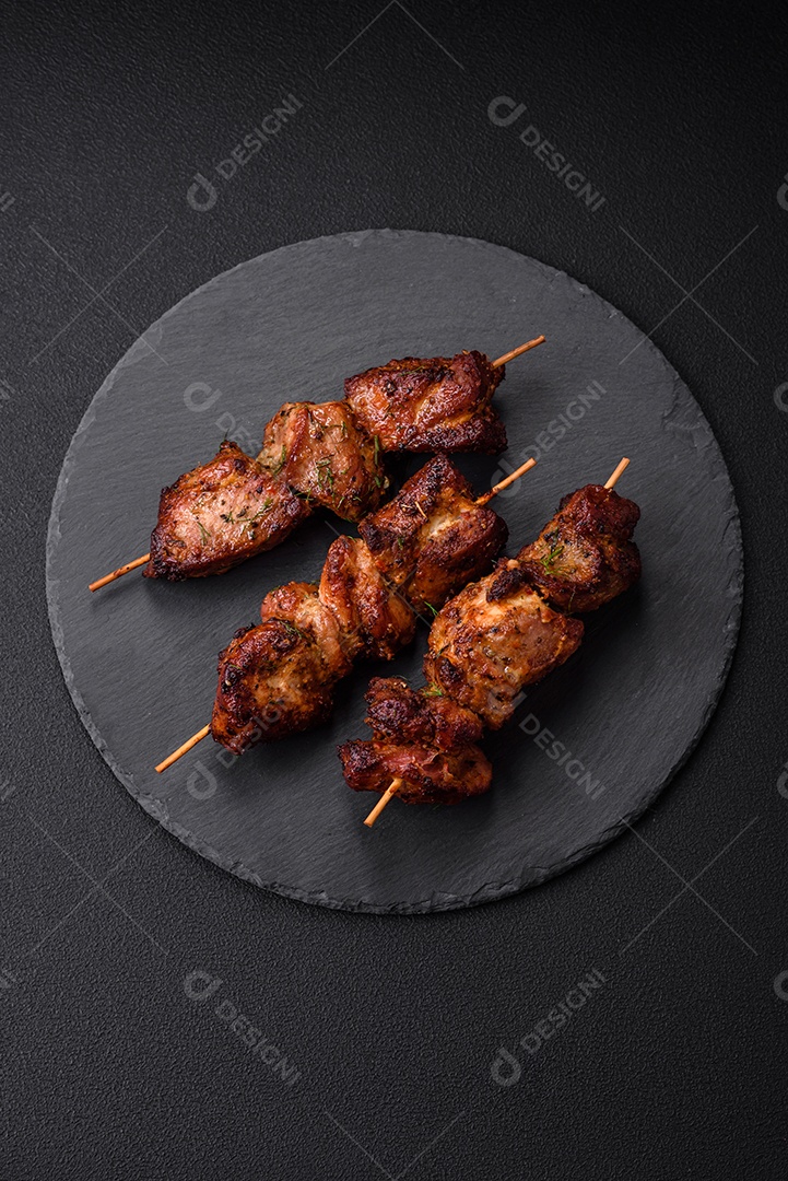 Deliciosos espetos de frango, peru ou porco grelhados com sal, especiarias e ervas no fogo sobre um fundo escuro de concreto