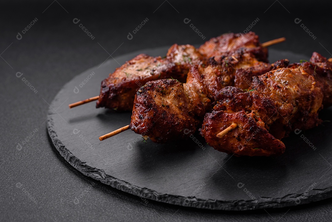 Deliciosos espetos de frango, peru ou porco grelhados com sal, especiarias e ervas no fogo sobre um fundo escuro de concreto