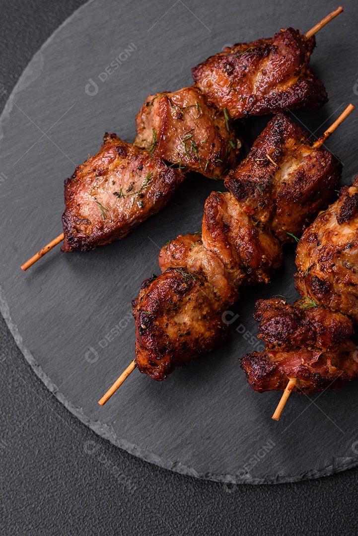 Deliciosos espetos de frango, peru ou porco grelhados com sal, especiarias e ervas no fogo sobre um fundo escuro de concreto