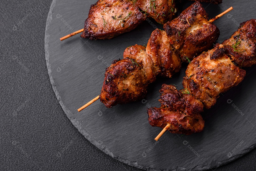 Deliciosos espetos de frango, peru ou porco grelhados com sal, especiarias e ervas no fogo sobre um fundo escuro de concreto