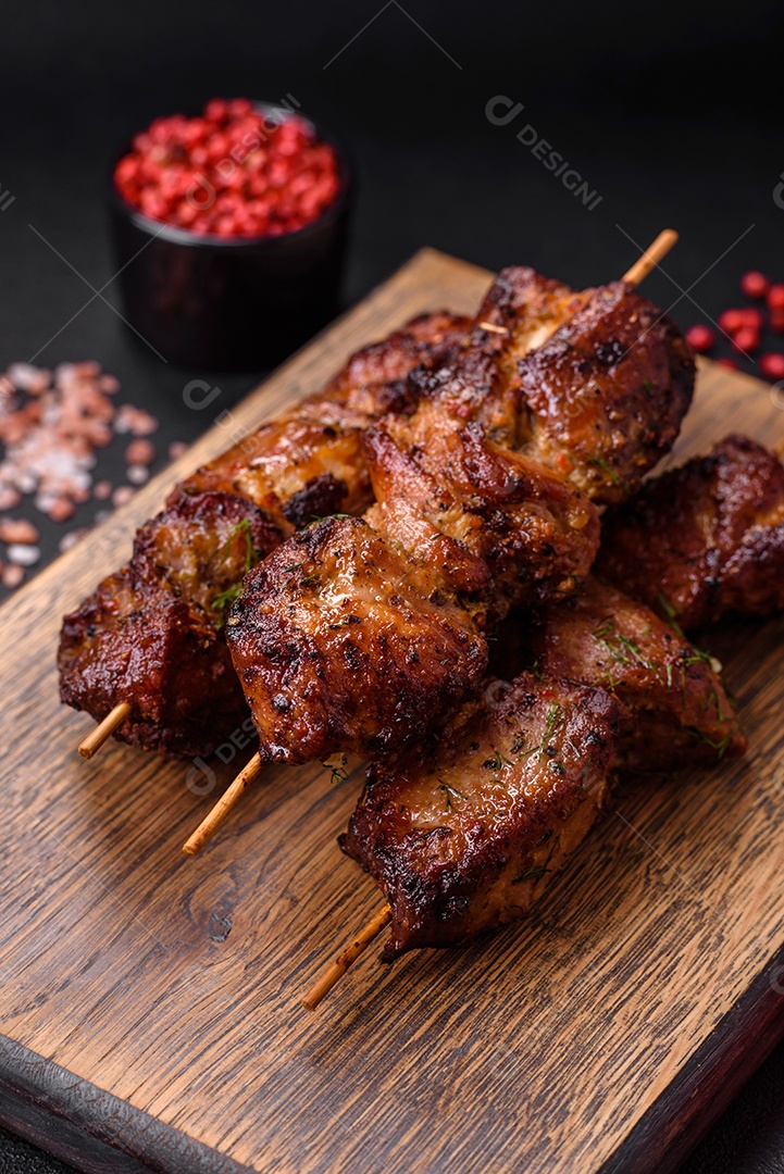 Deliciosos espetos de frango, peru ou porco grelhados com sal, especiarias e ervas no fogo sobre um fundo escuro de concreto