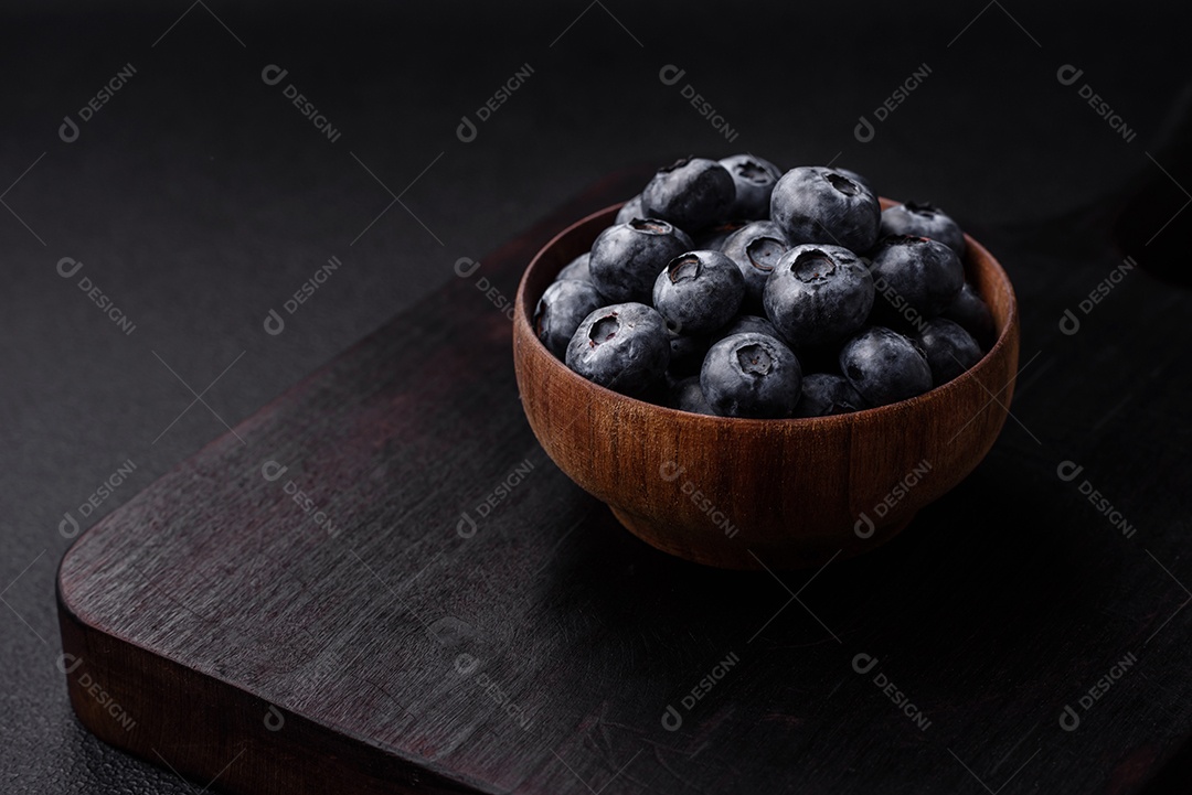 Deliciosos mirtilos doces frescos em uma tigela de cerâmica sobre um fundo escuro de concreto