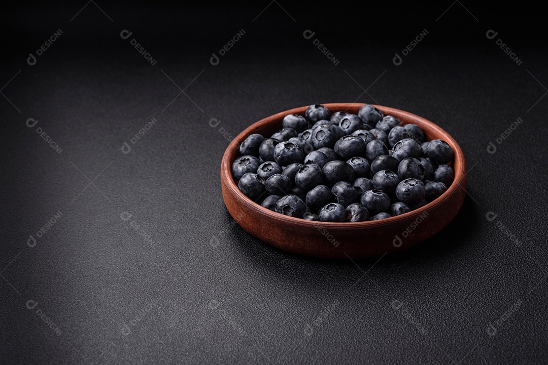 Deliciosos mirtilos doces frescos em uma tigela de cerâmica sobre um fundo escuro de concreto