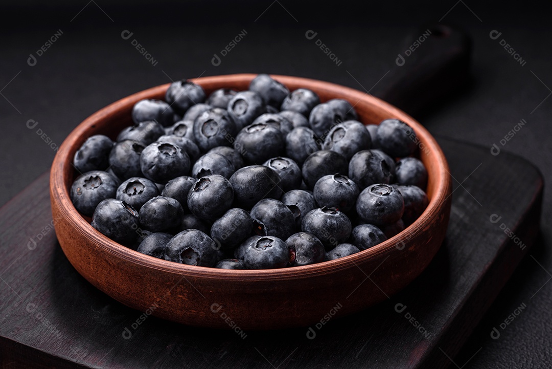 Deliciosos mirtilos doces frescos em uma tigela de cerâmica sobre um fundo escuro de concreto